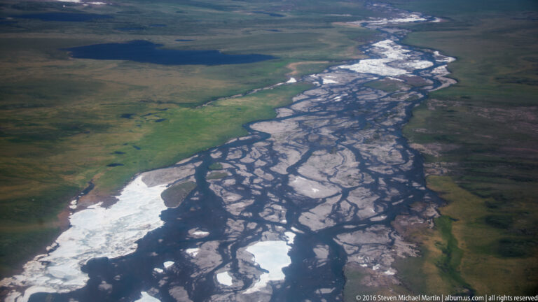 Dark river channels branch around pale gravel bars in a close overhead view.