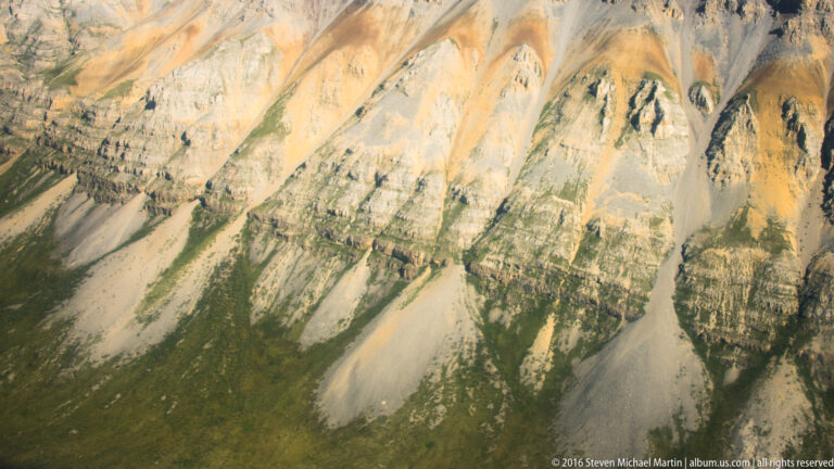 Close view of an ochre and pale rock face cut by narrow erosion channels.