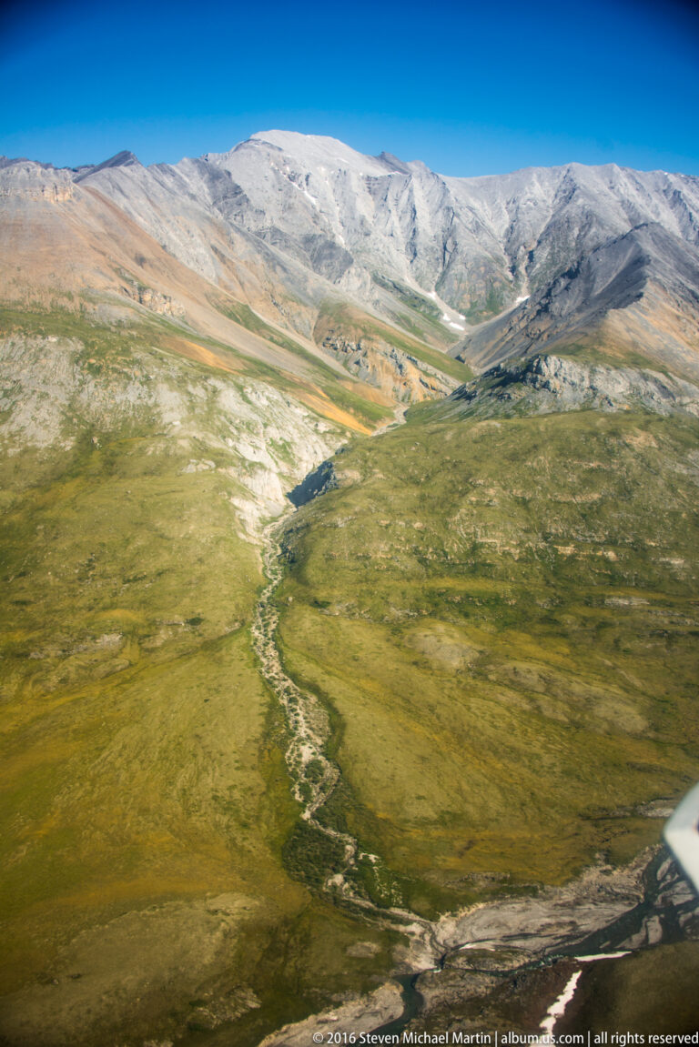 A branching stream crosses an open tundra basin below pale treeless mountains.