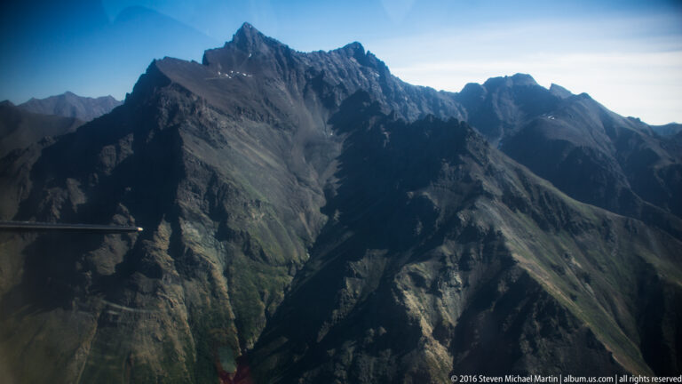 Jagged mountain peaks and deep shadowed gullies rise close beneath a pale sky.
