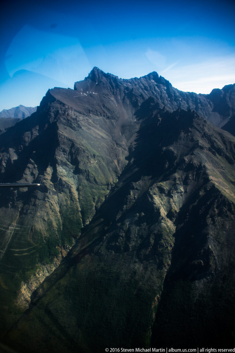 Dark foreground ridges lead toward sunlit mountains and a valley beneath blue sky.