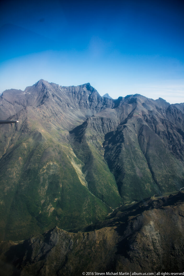 Rounded green mountain ridges recede toward distant peaks under a clear blue sky.