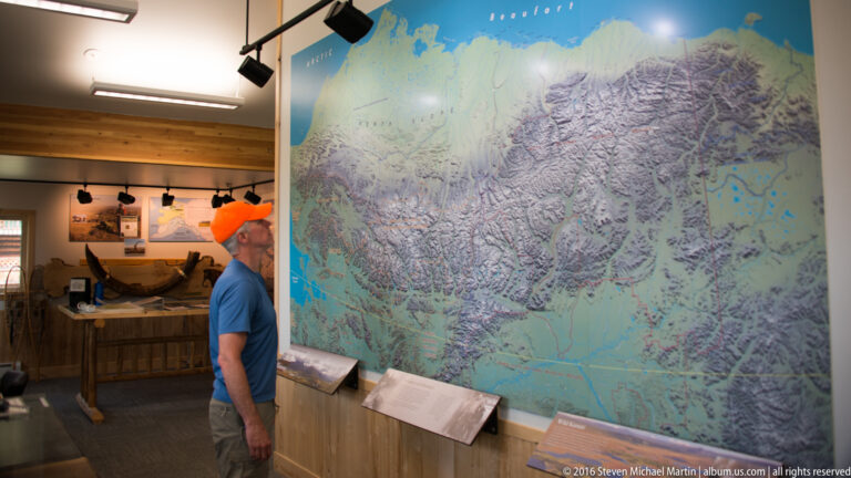 A visitor in an orange cap studies a large wall map in a wood-paneled exhibit room.