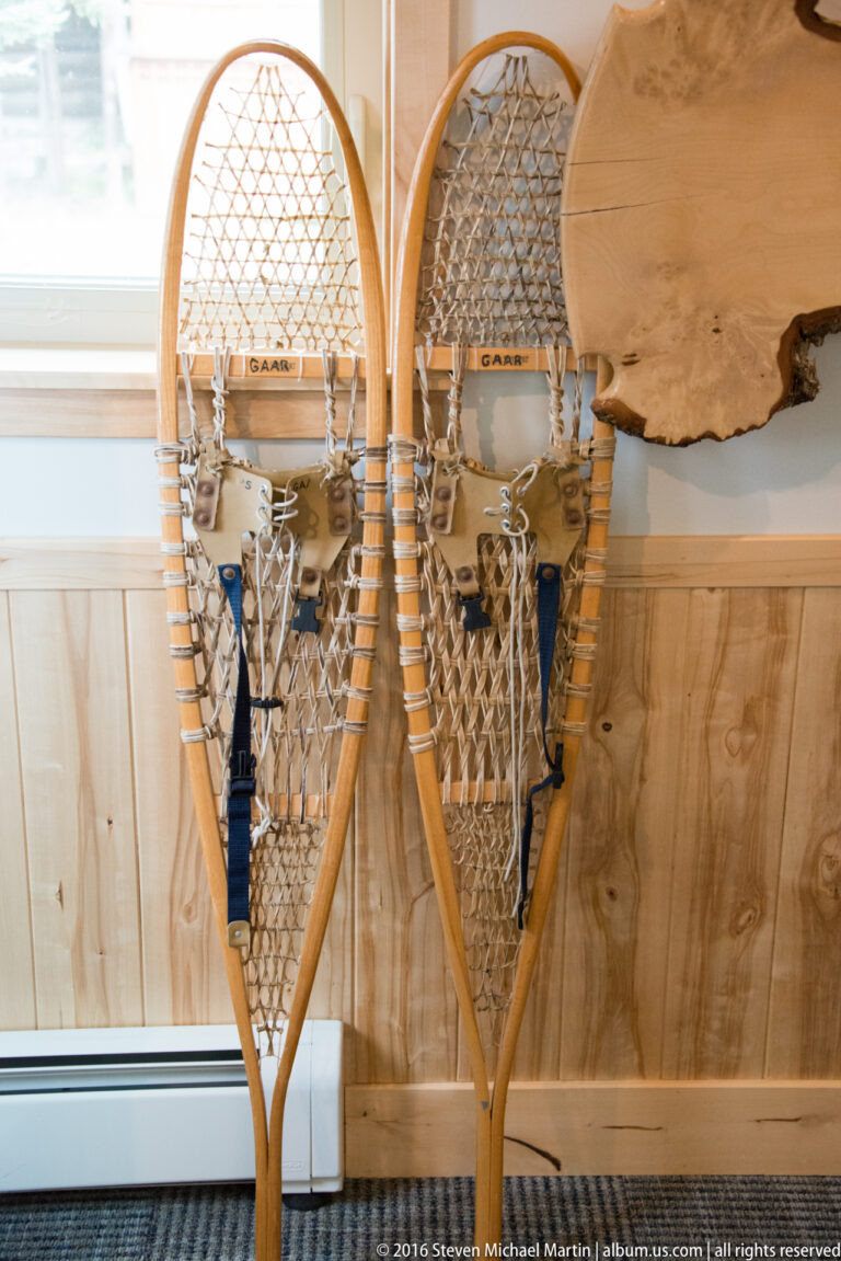 Two wooden-framed snowshoes with woven webbing hang on a pale paneled display wall.