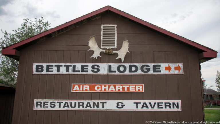 Wooden gable with signs for Bettles Lodge, air charter, restaurant, and tavern.