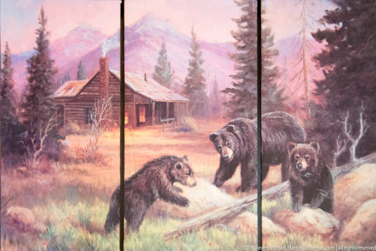 Three-panel painting of a log cabin, forest, and brown bears including cubs.