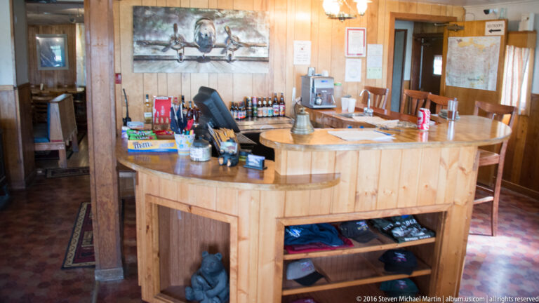 Wood-paneled lodge interior with a curved counter, chairs, maps, and visitor materials.