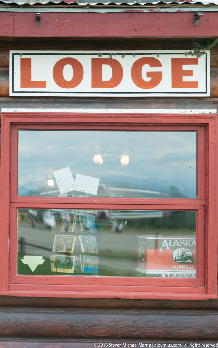 Red-framed lodge window beneath a sign reading LODGE, reflecting the outdoor surroundings.