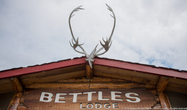 Large antlers mounted above the Bettles Lodge sign at the roof peak against a cloudy sky.