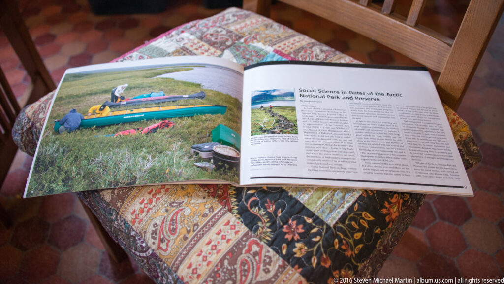 An open Arctic Alaska book lies on a patterned table, showing a canoe photograph beside a chapter about social sciences in the park.