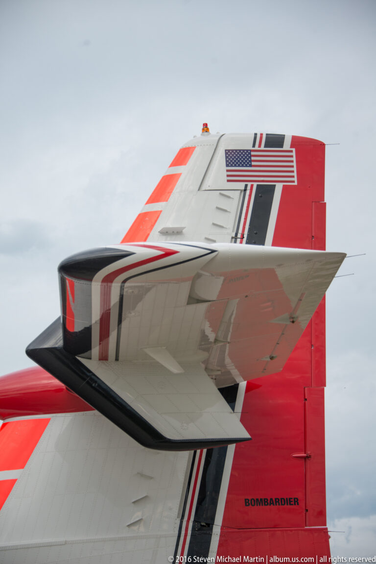 A red-and-gray aircraft wing crosses the frame beneath a tail marked Bombardier and a United States flag.