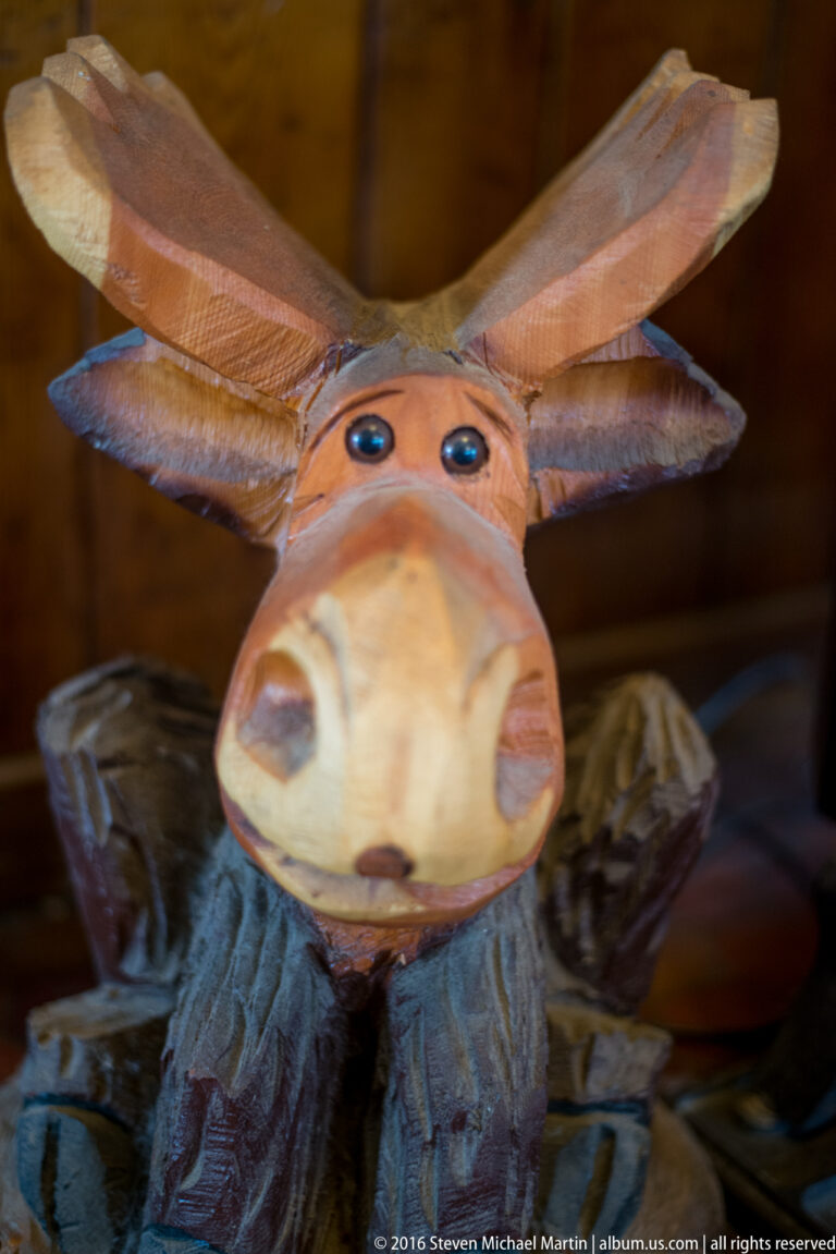 A carved wooden moose figure with raised antlers, a broad muzzle, and painted dark eyes fills the frame.