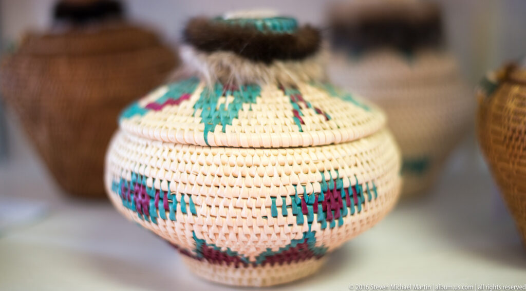 A small pale lidded basket has a looped top and turquoise and magenta geometric bands.
