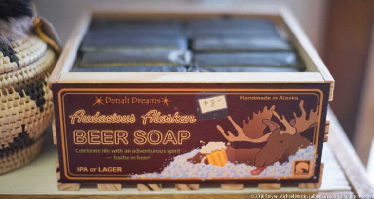 Bars in a wooden display box are labeled “Adventurous Alaskan Beer Soap” beside a cartoon moose.