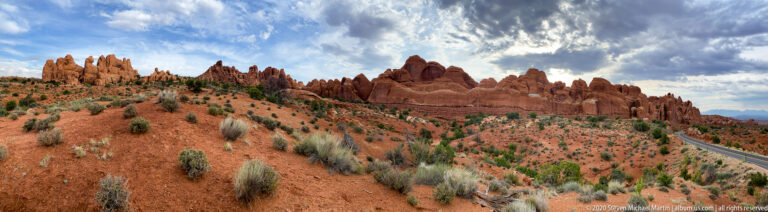 Red sandstone fins rise above desert scrub beside a curving park road.