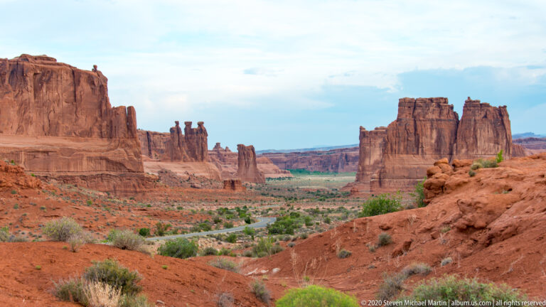Sandstone towers flank a broad valley with a road and green vegetation below.