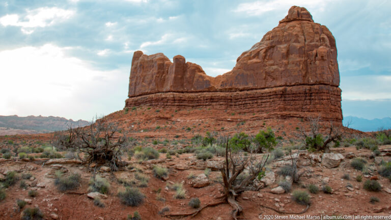 A blocky red sandstone butte with a cleft summit rises above a scrub plain.