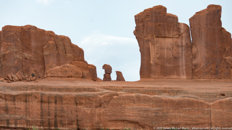 Two narrow sandstone pinnacles rise between larger walls above a layered rock bench.