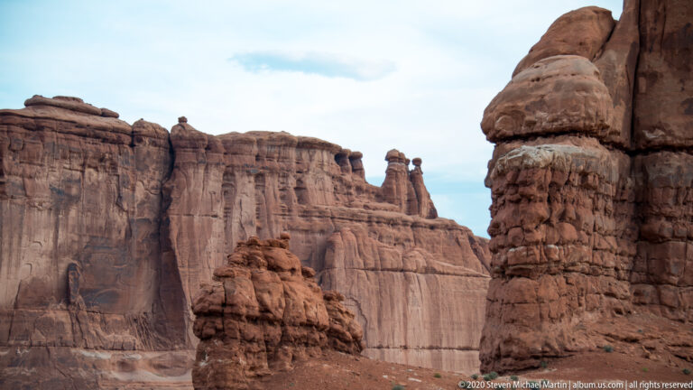 A narrow sandstone spire stands between tall cliffs above a small patch of canyon floor.