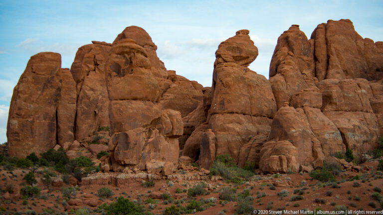 Rounded sandstone pinnacles rise above low shrubs beneath a lightly clouded sky.