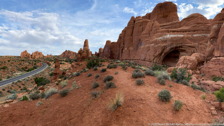A rounded opening cuts through a sandstone wall beside a winding park road.