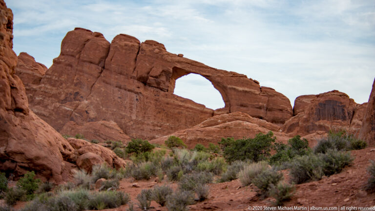 A broad natural opening cuts through a red sandstone ridge above desert vegetation.