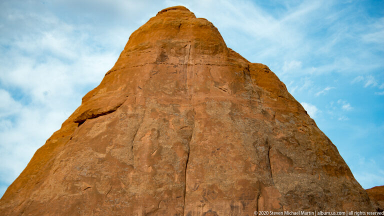 A broad sandstone tower rises close overhead, showing vertical cracks beneath a blue sky.