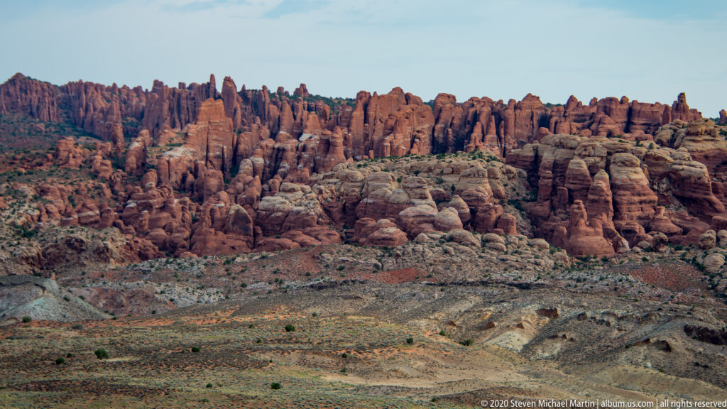 A continuous ridge of red sandstone fins rises above a pale open basin.