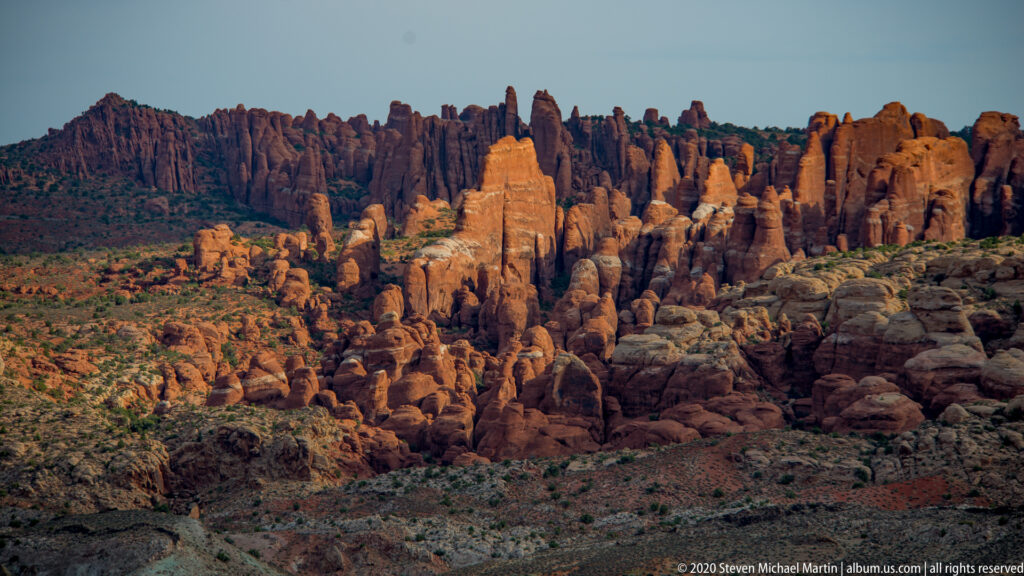 A sunlit sandstone tower stands amid darker fins and broken red rock.