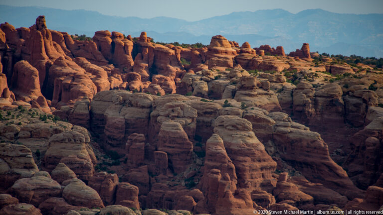 Rows of rounded sandstone fins and pinnacles extend toward distant blue mountains.