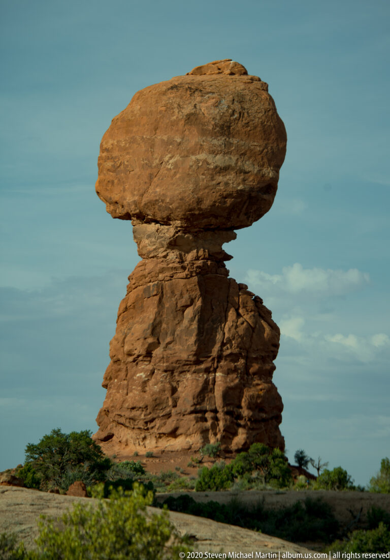 A broad sandstone capstone balances on a narrower pedestal above low desert shrubs.