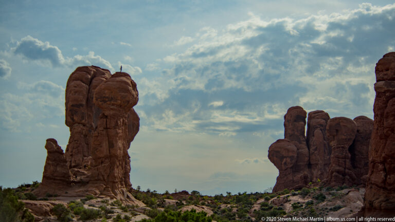 Two clusters of sandstone towers frame an open gap beneath textured clouds.