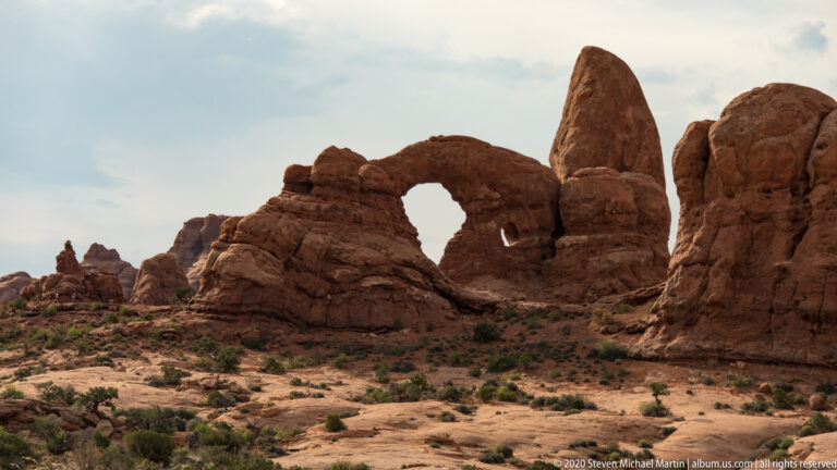 Rounded opening in a sandstone arch with a smaller hole below and a tall fin to the right.