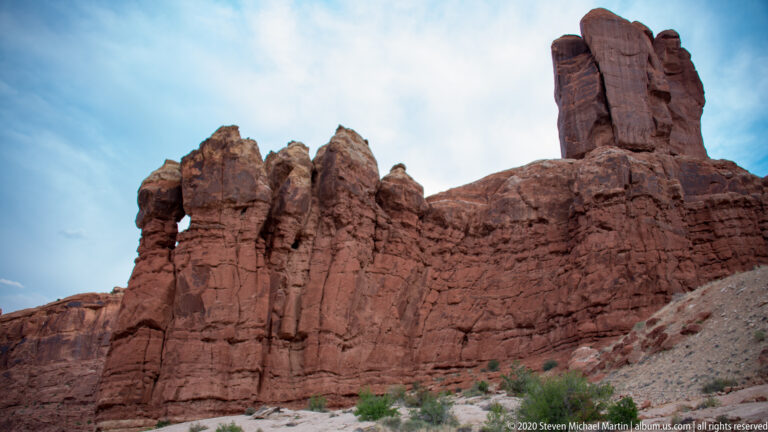 A small opening punctures a steep sandstone ridge below several blocky towers.