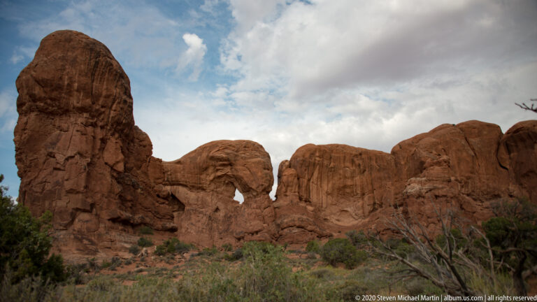 Narrow sandstone opening between a tall isolated fin and a broad rock wall.