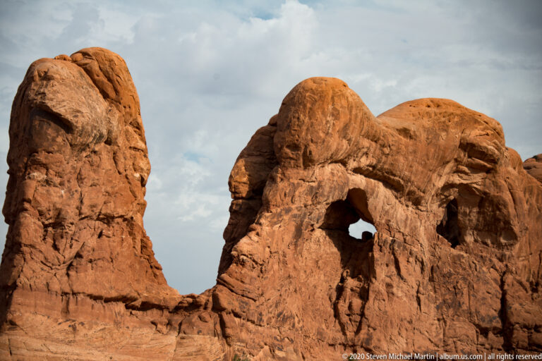 Small irregular opening in a rounded sandstone formation beside a taller rock column.