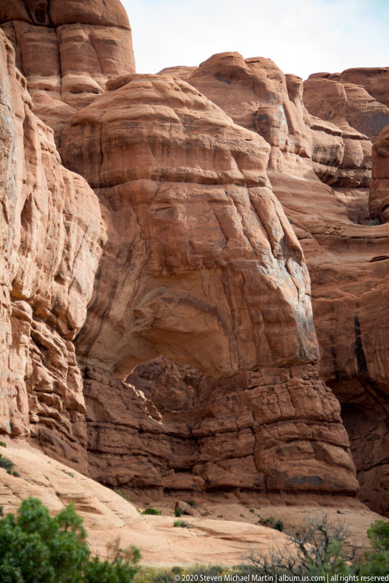 Layered sandstone wall with curved erosion lines and a shallow recess above a pale slickrock shelf.