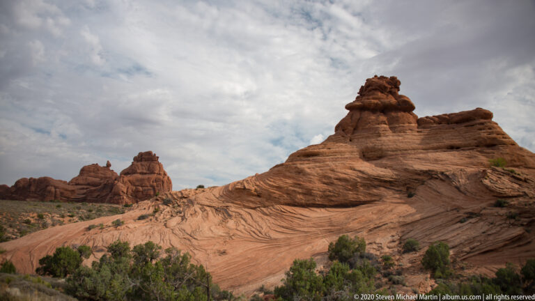 Rounded sandstone dome with a dark cap above a smooth, sparsely vegetated rock slope.
