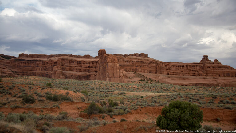 Long sandstone escarpment and isolated rock tower above a broad basin of desert shrubs.