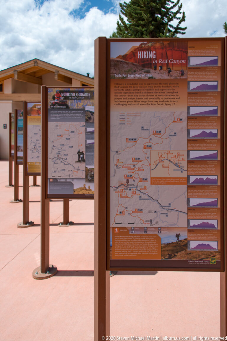 A “Hiking Red Canyon” panel with a trail map and elevation profiles stands in a plaza.