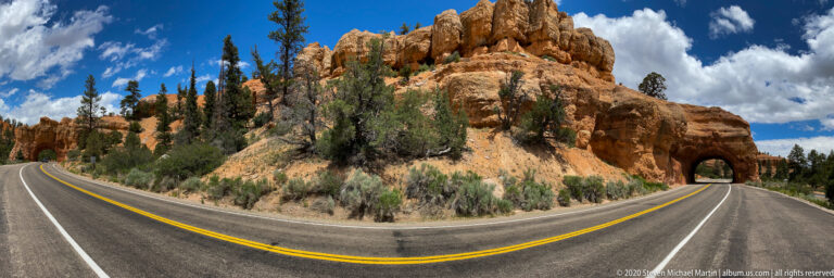 A curving two-lane road enters a tunnel cut through a red sandstone slope.