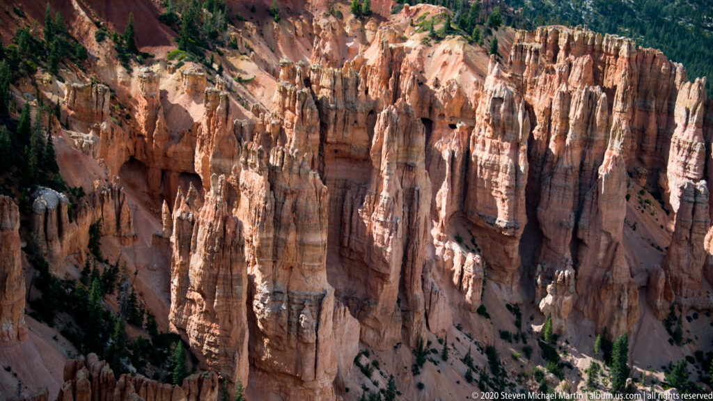 Close view of orange hoodoos with banded faces, narrow gullies, and small evergreen patches.