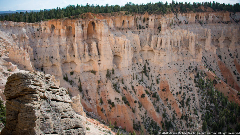 Pale foreground rock overlooks a cream and orange cliff carved with channels and small hollows.