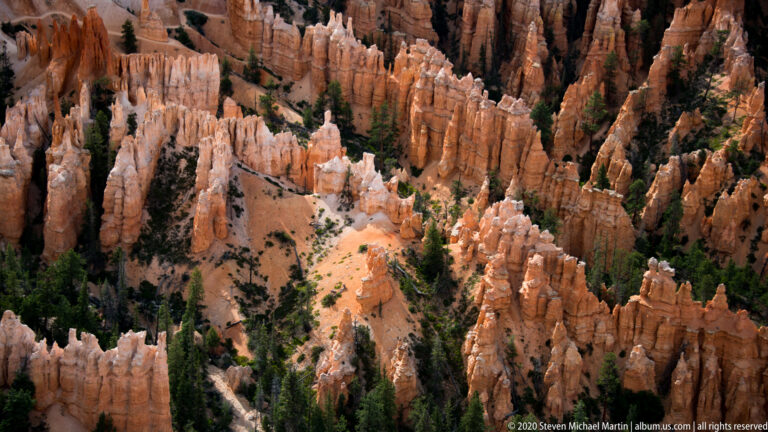 Sandy route descends between tightly grouped orange hoodoos and pale fins into the canyon.