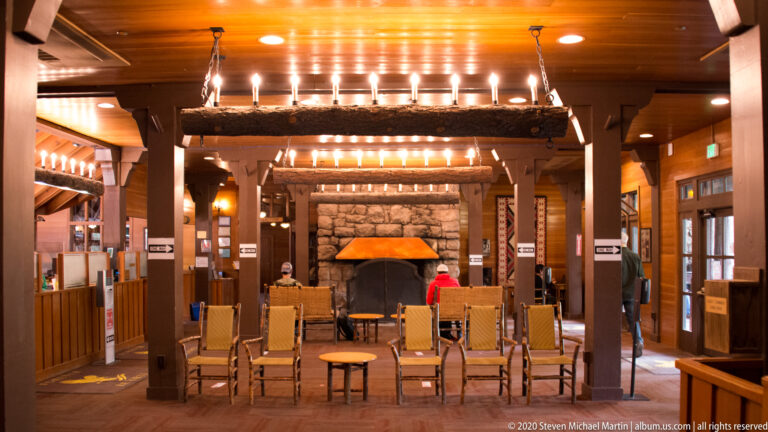 Stone fireplace and armchairs sit beneath a timber ceiling lined with pendant lights.