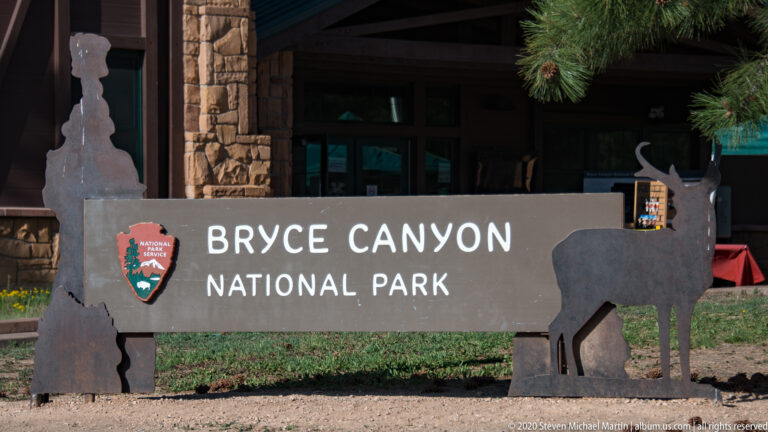 Bryce Canyon National Park sign with NPS emblem and bison silhouettes in front of a timber building.
