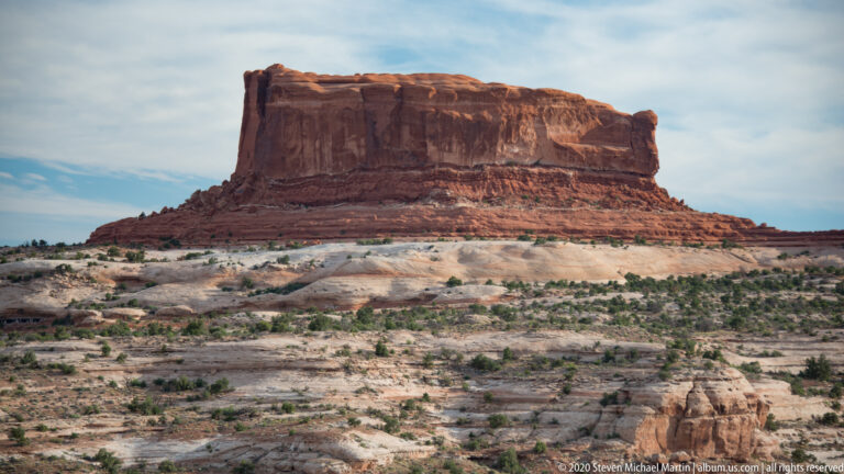 A broad sandstone butte rises above pale rock and sparse shrubs.