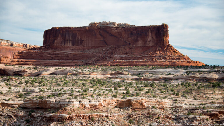 A sheer-sided mesa towers above stratified slopes and scattered vegetation.