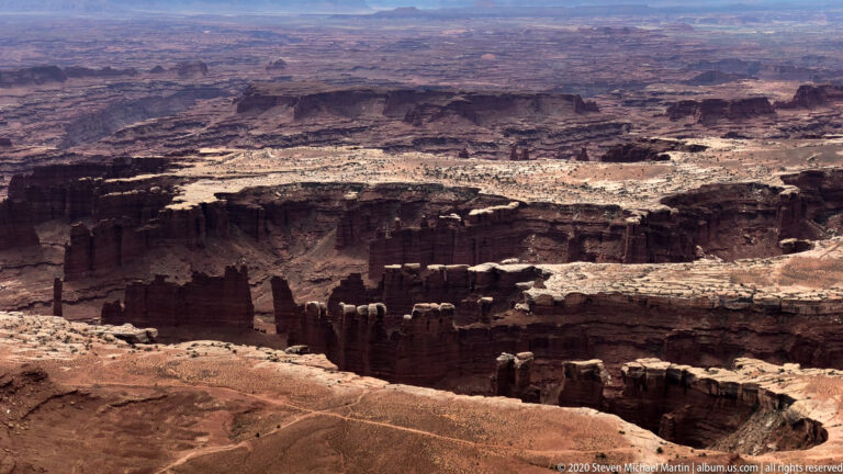 Dark cliffs and pale benches divide the distant canyon basin into layered terraces.