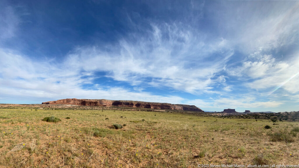 Clouds stream over a long mesa and open grassland.